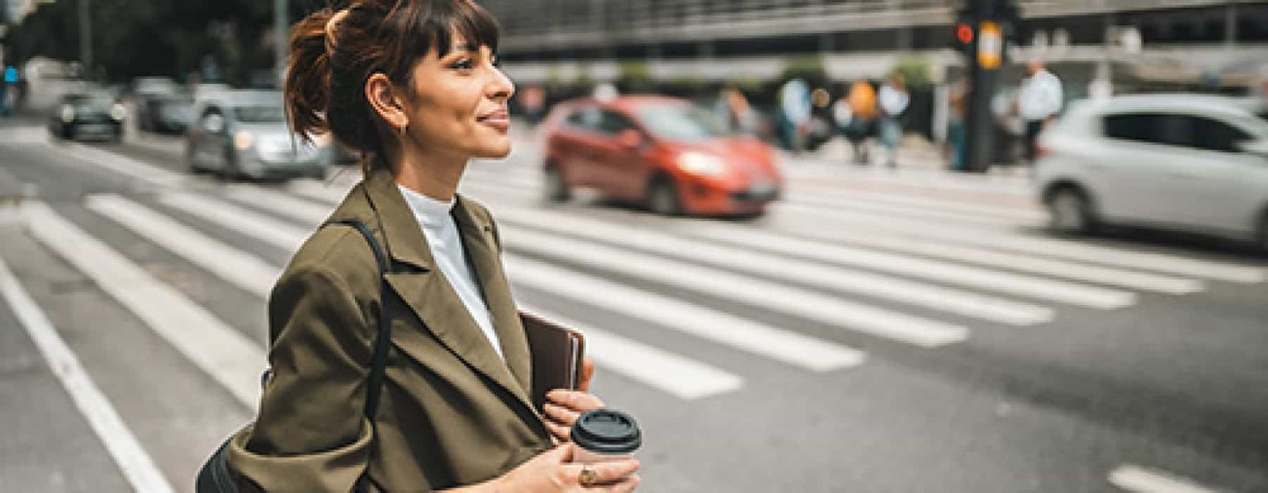 a person crossing the street holding a coffee